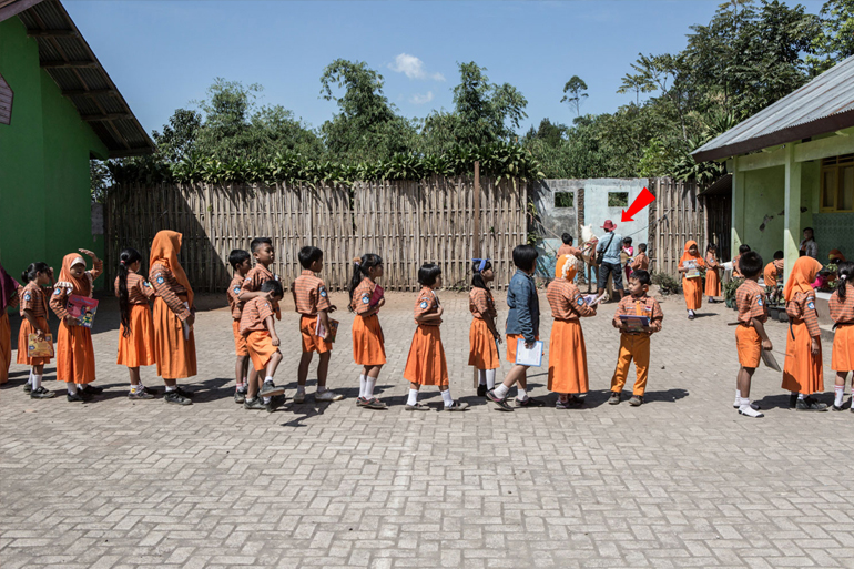 Παιδιά περιμένουν υπομονετικά να παραλάβουν ένα βιβλίο -  Στο βάθος ο 42χρονος Ridwan Sururi