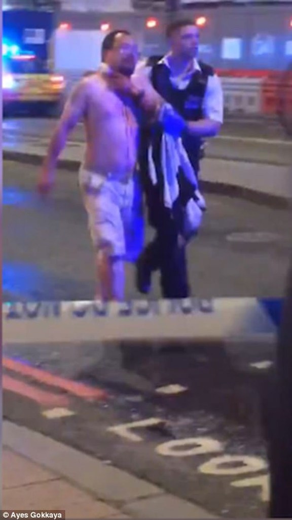 Ο δημοσιογράφος Geoff Ho μεταφέρεται σε ασθενοφόρο από έναν διασώστη που κρατά με δύναμη ένα πανί στο λαιμό του προκειμένου να σταματήσει την αιμορραγία μετά την επίθεση με μαχαίρι που δέχθηκε από έναν εκ των τριών ενόπλων/πηγή: Daily Mail