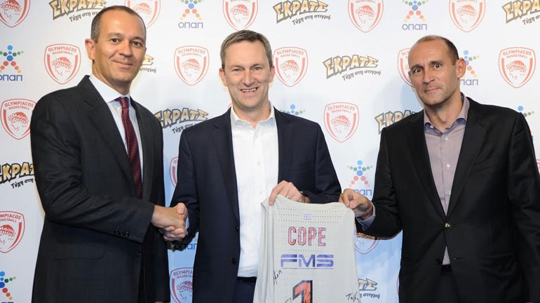 Οι κκ. Αγγελόπουλοι προσφέρουν στον Ντάμιαν Κόουπ, Διευθύνοντα Σύμβουλο ΟΠΑΠ, υπογεγραμμένη φανέλα της ομάδας του Ολυμπιακού