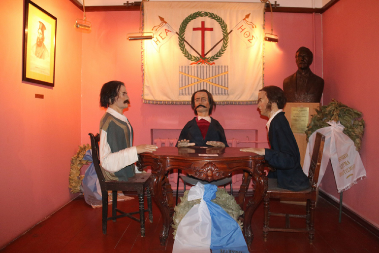 Τα τρία ιδρυτικά μέλη της Φιλικής Εταιρείας (Σκουφάς, Τσακάλωφ, Ξάνθος) κάθονται γύρω από ένα τραπέζι