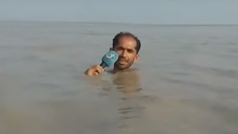 Σκληροτράχηλος Πακιστανός ρεπόρτερ κάνει ρεπορτάζ βυθισμένος μέσα στην πλημμύρα