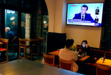 Άνθρωποι τρώνε σε εστιατόριο ενώ ο πρόεδρος Μακρόν απευθύνει τηλεοπτικό διάγγελμα