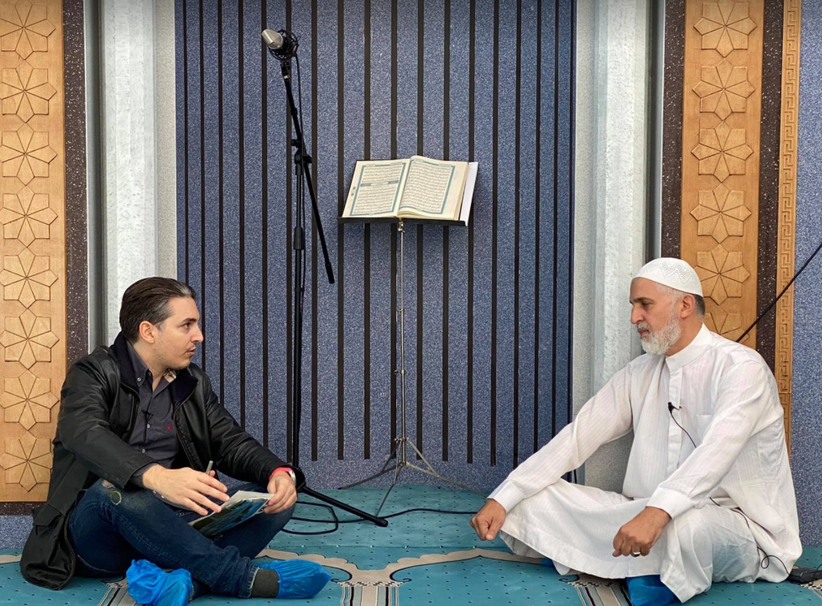Αριστερά ο ρεπόρτερ του zougla.gr , Xρήστος Μαζάνης με τον Ιμάμη, Σίντι Μοχάμεντ Ζακί κατά τη διάρκεια της συνέντευξης. Στο βάθος διακρίνεται το Κοράνι