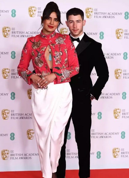 Η Priyanka Chopra Jonas με σύνολο Pertegaz floral bolero και ψηλόμεσο λευκό παντελόνι που συνδύασε με κοσμήματα από τον οίκο Bvlgari, ενώ δίπλα της ο Nick Jonas με tuxedo Giorgio Armani