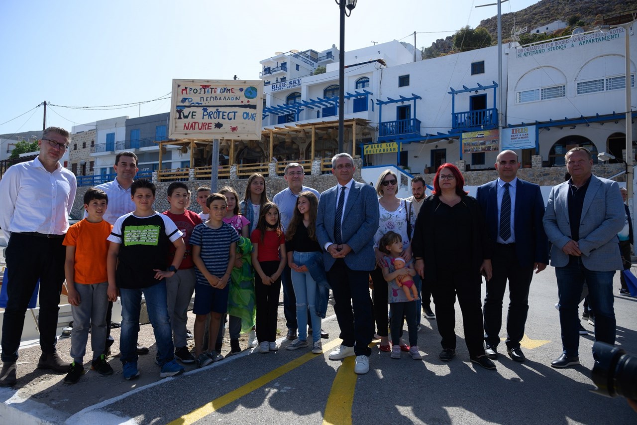 Ο Υπουργός Επικρατείας, κ. Άκης Σκέρτσος, ο Υπουργός Περιβάλλοντος και Ενέργειας, κ. Κώστας Σκρέκας, ο Γενικός Γραμματέας Συντονισμού Διαχείρισης Αποβλήτων του Υπουργείου Περιβάλλοντος κ. Μανώλης Γραφάκος, ο Περιφερειάρχης Νοτίου Αιγαίου κ. Γιώργος Χατζημάρκος, η Δήμαρχος Τήλου κα Μαρία Καμμά – Αλιφέρη και ο Ιδρυτής και Πρόεδρος της Polygreen κ. ΑθανάσιοςΠολυχρονόπουλος με μαθητές του Δημοτικού Σχολείου Τήλου μπροστά από την ταμπέλα που ετοίμασαν οι μαθητές.