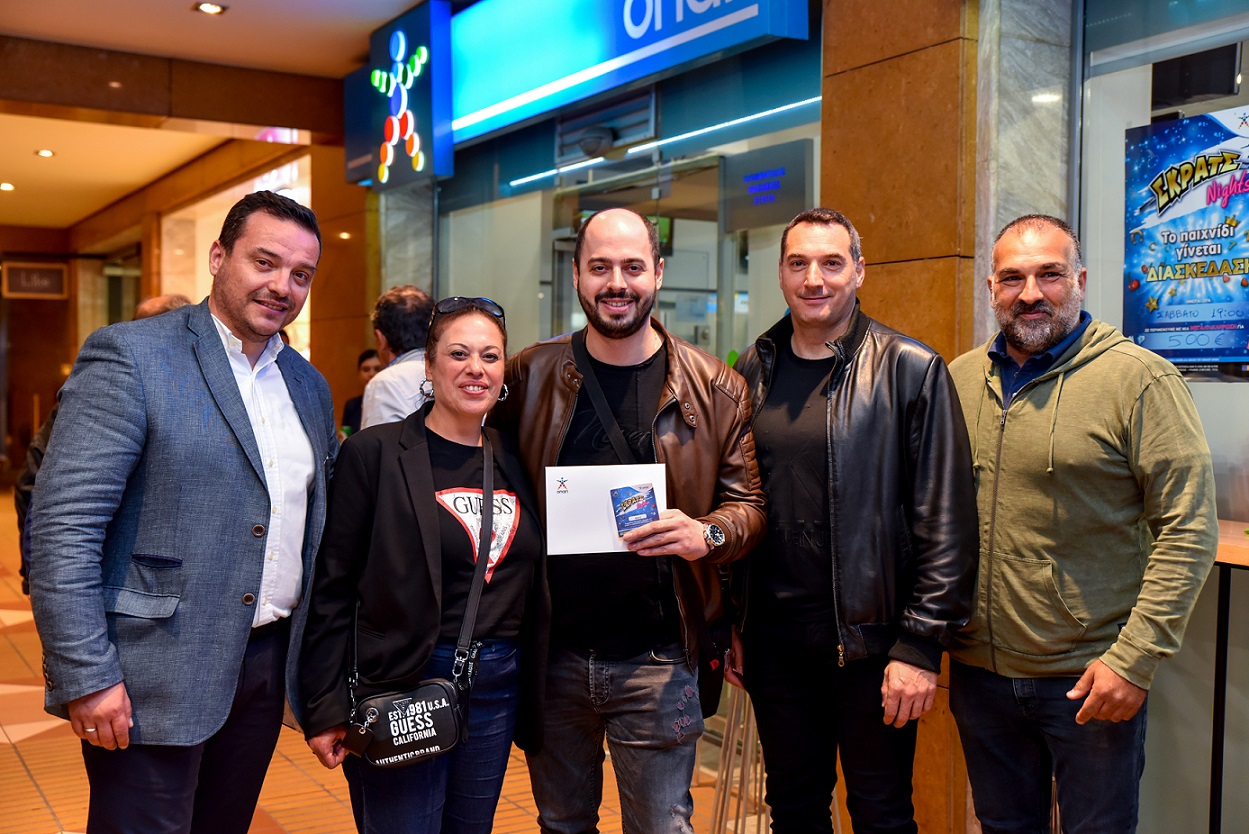 Ο νικητής της κλήρωσης με τον ιδιοκτήτη του καταστήματος ΟΠΑΠ και την ομάδα του ΟΠΑΠ.