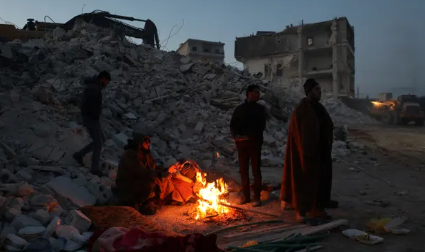 Επιζώντες ζεσταίνονται γύρω από μια φωτιά κοντά στο Ιντλίμπ της Συρίας / Πηγή: The Guardian