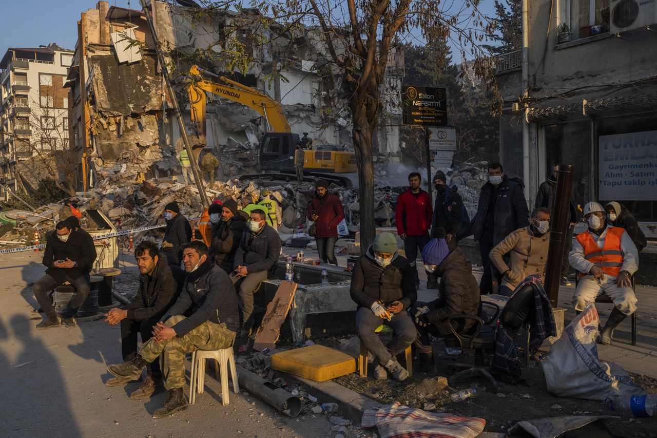 Οι άνθρωποι κάθονται δίπλα σε ένα κατεστραμμένο σπίτι καθώς περιμένουν να ανασυρθούν τα σώματα φίλων και μελών της οικογένειάς στην Αντιόχεια