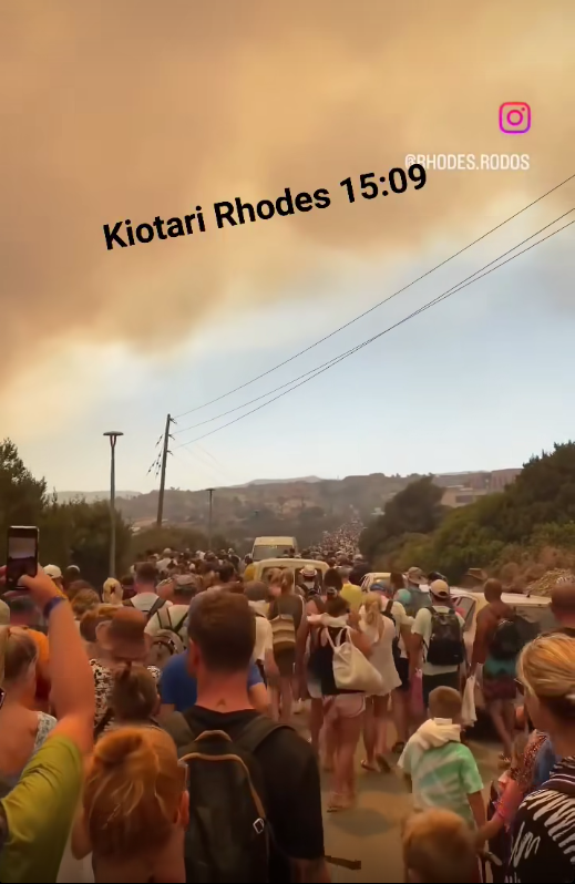 Εκατοντάδες άνθρωποι απομακρύνονται με τα πόδια ενώ ο ουρανός έχει καλυφθεί από ένα πυκνό σύννεφο καπνού